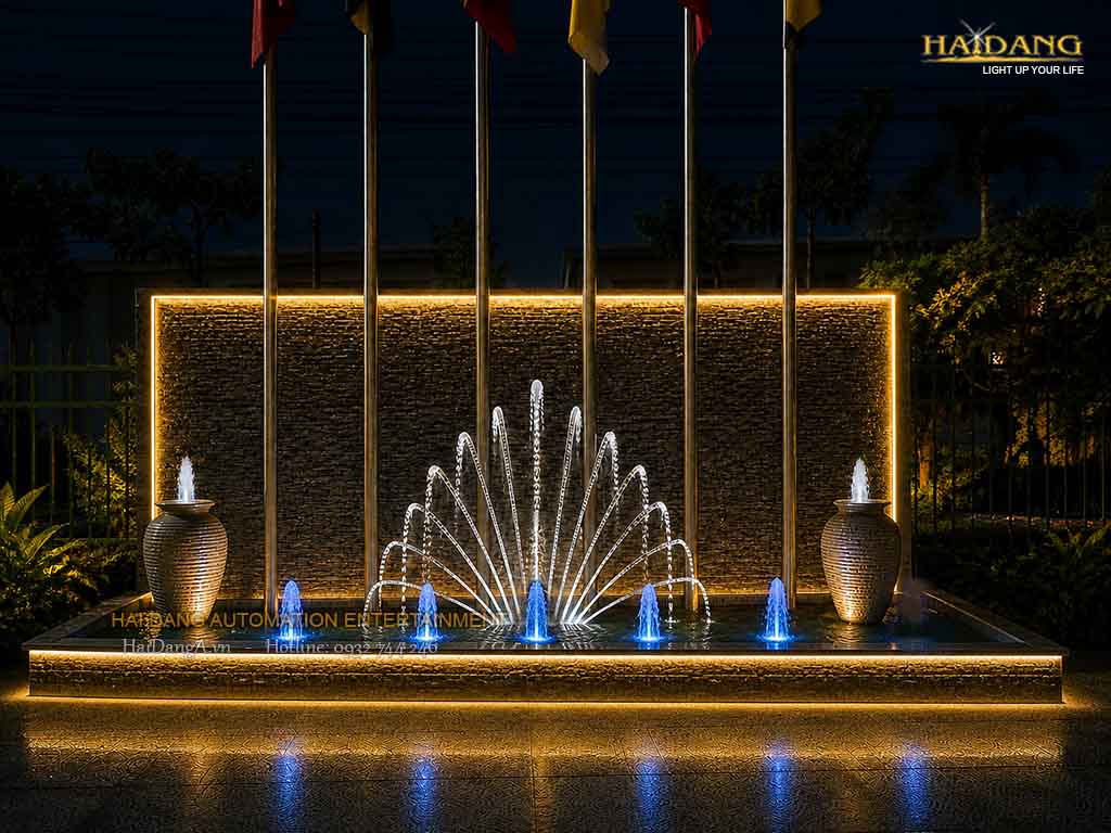 Đài phun nước cột cờ với cụm phun đuôi chim công và các vòi phun sủi bọt trong hồ và trên lu phun nước